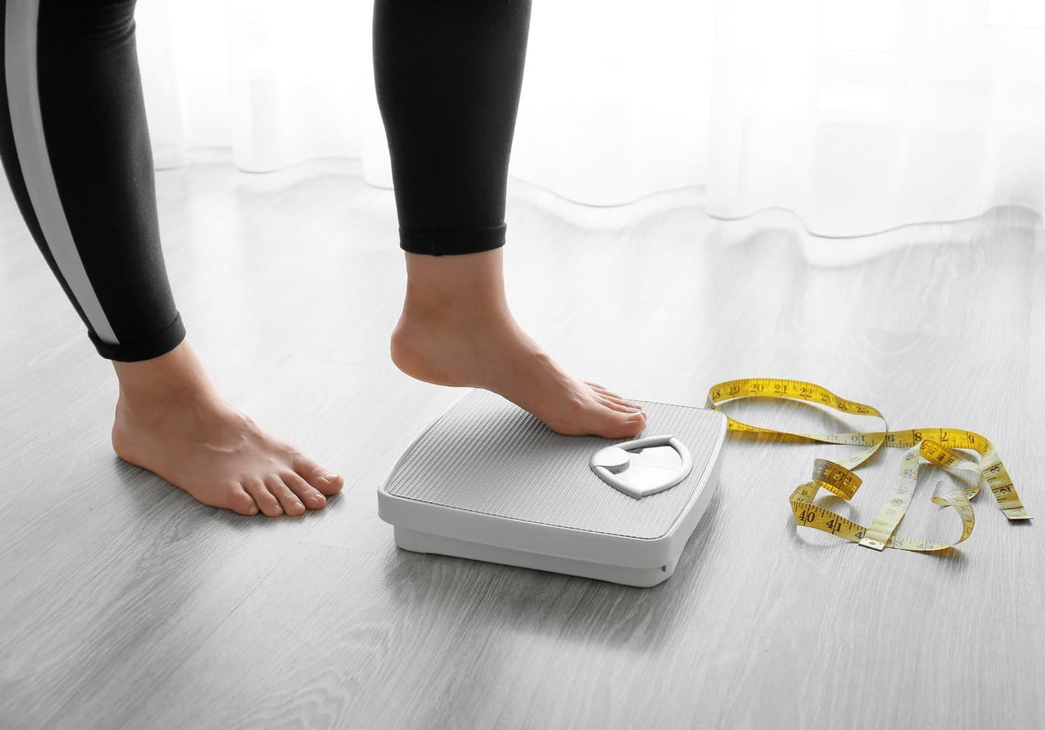 Stepping on a bathroom scale with measuring tape — body composition tracking goes beyond scale weight at Momentum Fitness NYC